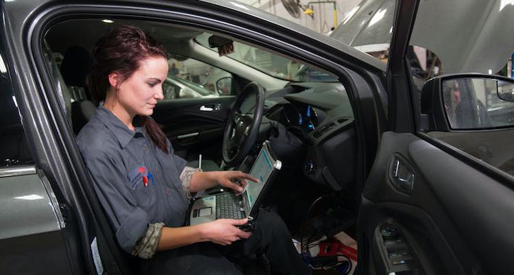 female automotive technology student running diagnostics on a laptop inside of a car